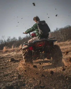 A person riding an ATV on a dirt trail, kicking up dust.